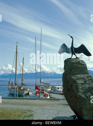 Sculpture métallique d'un skarv (cormorant), avec des voiliers amarrés dans le port au-delà, Harstad, Hinnøya, Troms, norvège arctique. Banque D'Images