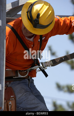 Le port de l'utilitaire workman harnais de sécurité et un casque de l'installation de nouveaux équipements sur une structure de sous-station électrique Banque D'Images