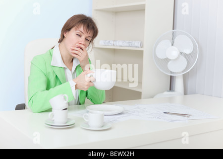 La femme fatiguée est assis à une table avec la grande tasse de café et bâillements Banque D'Images