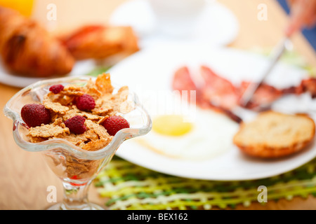 Délicieux petit-déjeuner servi. Flocons de maïs avec des baies, œuf frit, bacon, toasts, croissants, jus et café frais. Banque D'Images