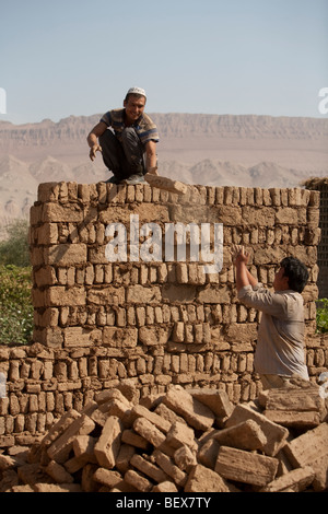 Les hommes ouïghours de construire le mur d'une maison neuve avec adobe briques de boue dans la région de Turpan, Chine. Banque D'Images
