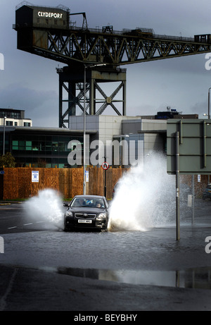 Une voiture roule sur une route inondée après de fortes pluies dans la région de Govan sur le côté sud de Glasgow, Ecosse. Banque D'Images