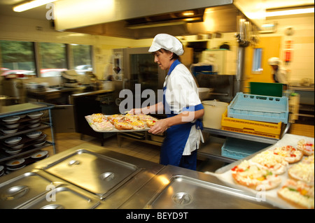 Femme cuisinier dans une cantine de l'école primaire à propos de cuisine pour cuire un bac de pizzas pour le déjeuner, UK Banque D'Images