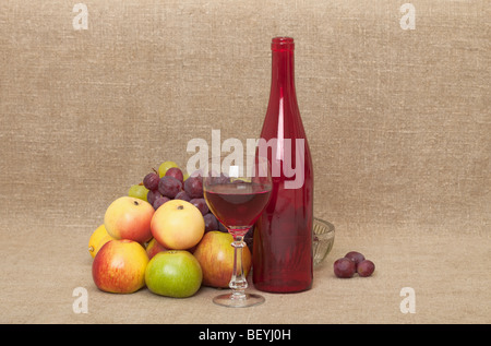 La nature morte sur une toile - une grande bouteille en verre rouge, un verre, pommes et raisins Banque D'Images