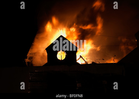 Apex de bâtiment de l'usine en feu dans la nuit avec des flammes en arrière-plan Banque D'Images