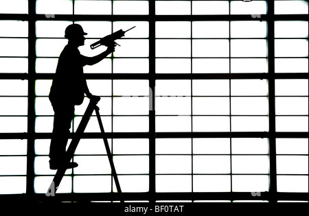 Un homme sur une échelle met la dernière main à un grand mur opaque dans le hall des départs de l'aéroport de Glasgow, en Écosse. Banque D'Images