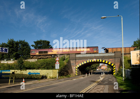 Train de fret roulant sur un pont de chemin de fer traversant une route dans les Midlands, Angleterre Banque D'Images