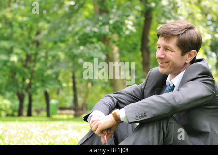 Les témoins de cette série - smiling Young business man de l'emplacement sur l'herbe verte et relaxing in park Banque D'Images