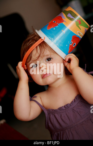 Image drôle d'un bébé de 18 mois fille portant un seau en plastique sur la tête. Banque D'Images