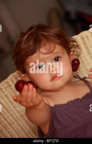 Dix-huit mois baby girl eating cherries Banque D'Images