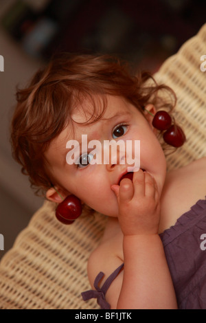 Dix-huit mois baby girl eating cherries Banque D'Images