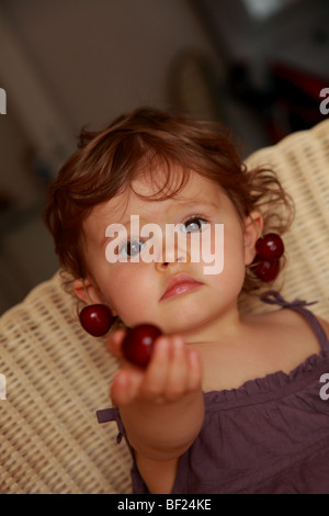 Faustine 18 mois holding cerises sur les oreilles Banque D'Images