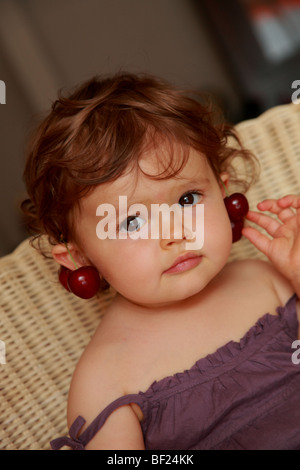 Faustine 18 mois holding cerises sur les oreilles Banque D'Images