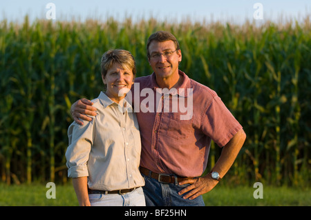 Agriculture - Mari et femme agriculteurs posent avec leur récolte de maïs grain venant à échéance dans l'arrière-plan / Minnesota, USA. Banque D'Images