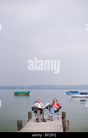 Vieux couple assis sur la jetée, lire un journal, le lac Ammersee, Bavière, Allemagne Banque D'Images