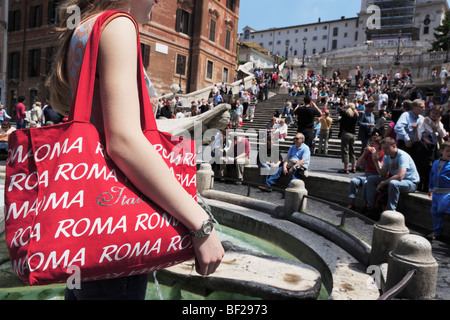 Jeune femme avec un sac rouge Roma à Fontana della Barcaccia sur la Piazza di Spagna, place d'Espagne en arrière-plan, Rome, Italie Banque D'Images