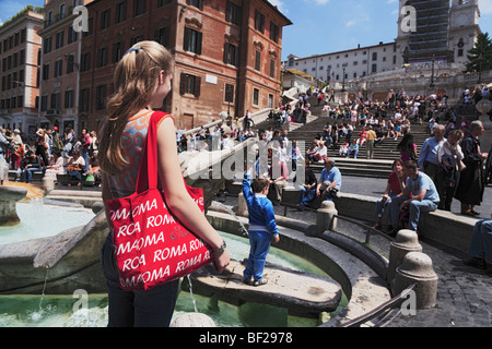 Jeune femme avec un sac rouge Roma à Fontana della Barcaccia sur la Piazza di Spagna, place d'Espagne en arrière-plan, Rome, Italie Banque D'Images