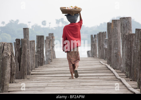 Les birmanes, vu de dos portant un panier sur sa tête en marchant sur le pont U Beins dans Amarapura près de Mandalay, M Banque D'Images