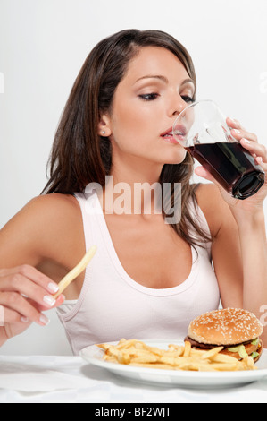 Femme buvant un cola avec hamburger et frites Banque D'Images