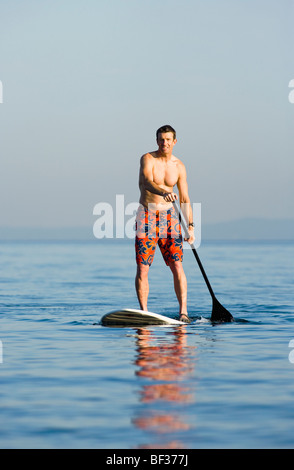 Fin des années 30 un homme de race blanche sur un stand up paddle board sur le Puget Sound près de Seattle, WA. Banque D'Images