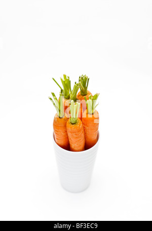 Sélection de jeunes carottes dans un pot blanc sur un fond blanc. Banque D'Images