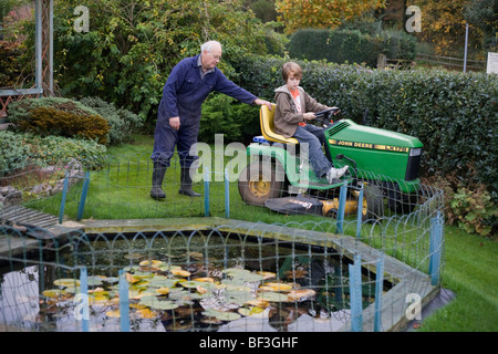 Supervisé par son grand-père, un garçon de 11 ans conduit son grand-père tracteur tondeuse dans le jardin familial. Banque D'Images