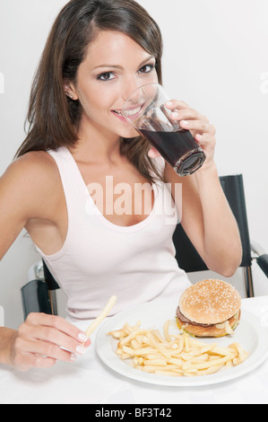 Femme buvant un cola avec hamburger et frites Banque D'Images