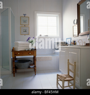 Les serviettes blanches sur la vieille table en pin blanc dans une salle de bains privative avec jonc de l'enfant assis-chaise à côté de coiffeuse Banque D'Images