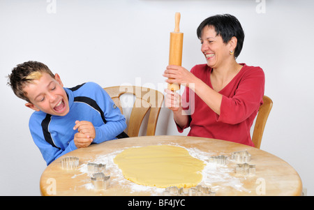 Noël cuisson, mère et fils rire ; pâte et emporte-pièce sont posé sur la table Banque D'Images