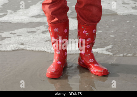 Les jambes avec un pantalon rouge et des bottes en caoutchouc rouge sur la plage de la mer du Nord, Vejer plage, Jutland, Danemark, Europe Banque D'Images