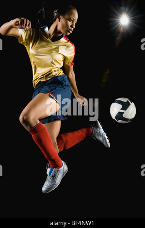 Race mixte soccer player kicking ball dans l'air Banque D'Images