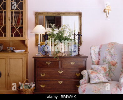 Miroir au-dessus de la lampe allumée et vase de fleurs sur la commode ancienne-de-tiroirs à côté aile florale-président de cottage salle de séjour Banque D'Images