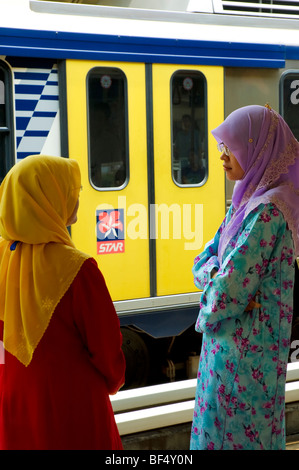 Femelle de couleur les navetteurs de hijab islamique chat pendant qu'ils attendent à une station. Kuala Lumpur, Malaisie Banque D'Images