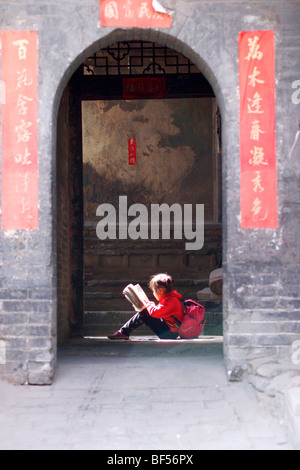 Girl reading dans l'embrasure d'une maison traditionnelle, Pingyao, Shanxi Province, China Banque D'Images