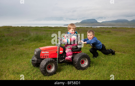 Jeune garçon en poussant sa jeune sœur sur tracteur jouet, Eskifjordur, Islande Banque D'Images