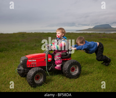 Jeune garçon en poussant sa jeune sœur sur tracteur jouet, Eskifjordur, Islande Banque D'Images