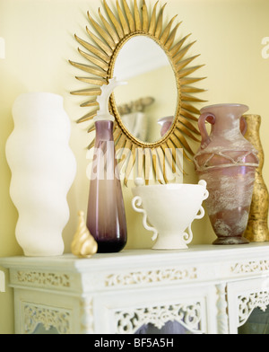 Sunburst doré miroir au-dessus de céramique blanche et mauve vases de verre sur blanc-manger Banque D'Images