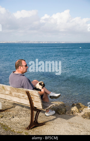 Un homme et son chien assis sur un banc au bord de la mer et profiter de la vue Banque D'Images