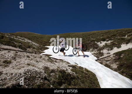 Riders vtt vélos transportant sur un champ de neige sur le sentier entre le Kreuzjoch gorge de montagne à la ju dles Cacagnar Banque D'Images