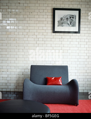 Coussin Rouge sur le fauteuil gris moderne contre un mur de briques en céramique blanche in modern living room Banque D'Images