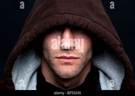 Un mal à un homme portant un haut à capuchon avec ses yeux dissimulés sur un fond noir. Banque D'Images