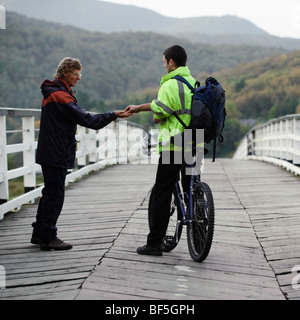 Un cycliste le péage-keeper de traverser l'ancien pont à péage de propriété privée en bois à l'estuaire de Mawddach Penmaenpool, UK Banque D'Images