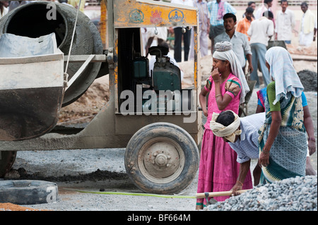 Les femmes indiennes debout à côté d'une grande bétonnière tout en travaillant sur les routes à Puttaparthi, Andhra Pradesh, Inde. Banque D'Images