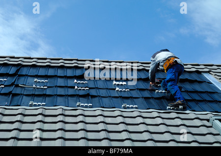 Travailleur enlevant des tuiles de toit et installant des panneaux Intersol imperméables pour panneaux solaires photovoltaïques sur une maison privée Banque D'Images
