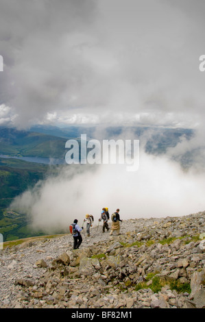 Marcheurs utilisant des bâtons de randonnée sur le chemin rocheux, au-dessus des nuages sur Ben Nevis avec Loch Eil au loin. Écosse Banque D'Images