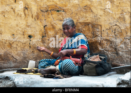 Femme indienne ancienne réparation maroquinerie assis sur la rue qui est couvert de poudre décolorante dans Puttaparthi, Andhra Pradesh, Inde Banque D'Images