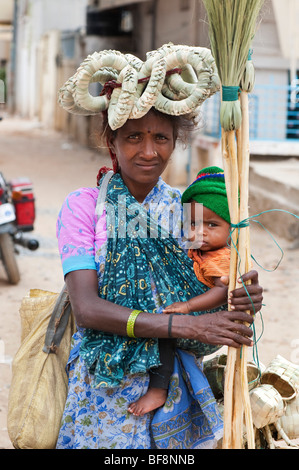 La mère et l'enfant indien fait main vente pinceaux et paniers en pot se dresse sur sa tête. Puttaparthi, Andhra Pradesh, Inde Banque D'Images