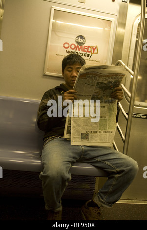 L'homme chinois lit un journal chinois sur une rame de métro de la ville de New York. Banque D'Images