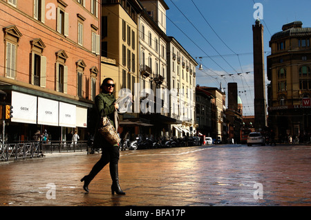 Femme traverse la rue Via Francesco Rizzoli avec la tour Asinelli, derrière l'un des deux tours de Bologne à Bologne Italie Banque D'Images