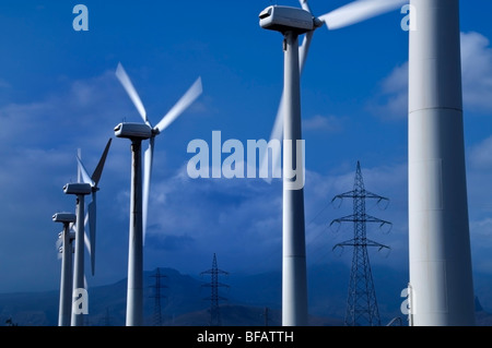 Ferme éolienne générant des pylônes électriques et d'économie avec des montagnes et nuages ciel derrière Banque D'Images